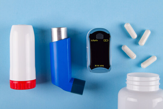Top view of oximeter, bottle of pills and inhalers on blue background with. Concept of Tight chest feeling caused by asthma