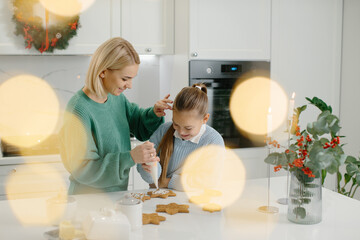Mother and daughter prepare Christmas cookies and decorate them with icing for a merry Christmas...
