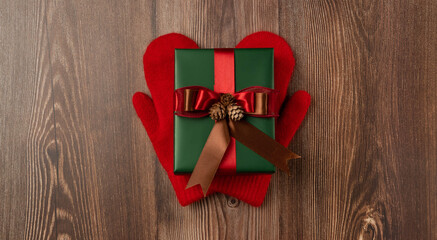 Christmas gift box with red ribbon on red mittens. Top view