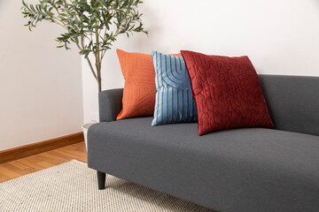 Scandinavian interior decoration of grey sofa with blue, red and orange pillow on it. Green plant...