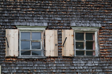 old farmhouse facade cladded with wood shingles and two windows with shutters
