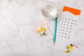 Vitamins and supplements. Variety of vitamin tablets with a glass of water and a calendar on a texture background. Multivitamin complex for every day. Nutritional supplements.