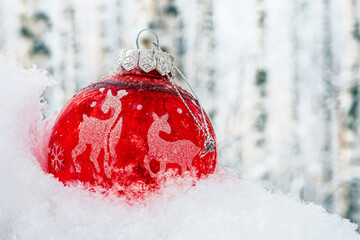 A red ball with deer drowned in a snowdrift in the winter forest. Christmas concept