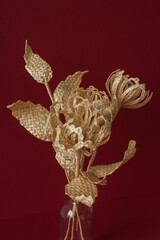 A glass vase with a bouquet of flowers made from straw on the red background.