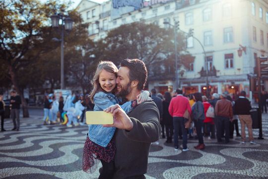 Father and Daughter Taking a Selfie in a Busy City Square