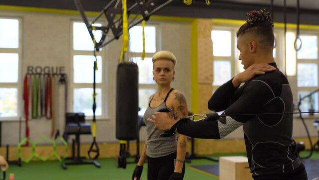 Male sport coach explaining to young woman how to training with cable crossover machine at gym. Attractive woman working out with personal coach.