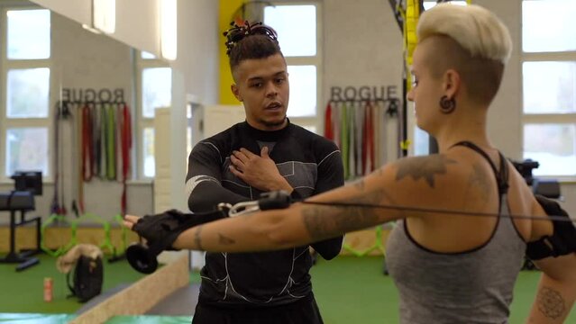 Male sport coach explaining to young woman how to training with cable crossover machine at gym. Attractive woman working out with personal coach.