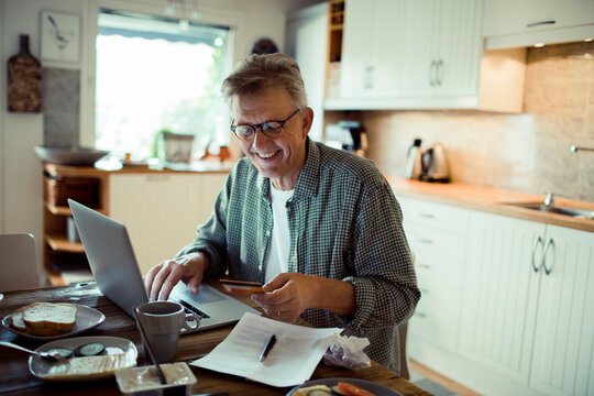 Smiling mature senior man paying bills online with credit card