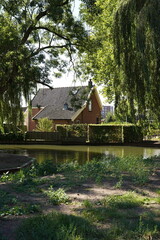 A quaint cottage nestles by the water's edge, framed by overhanging willows in a serene Dutch setting