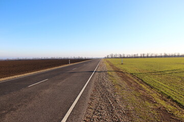 Fototapeta na wymiar Asphalt road near agricultural fields and blue sky on a backround