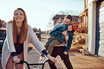 Happy parents teaching little son to ride a bike outside