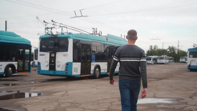 Following back shot of young man walking through trolleybus parking. Driver in casual clothes heading to blue electric vehicle to start working day