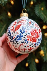 Closeup of a Christmas bauble with hand painted hygge pattern on it, Christmas colors. Hand is holding a white bauble. New Year's concept.