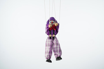 The frame features a puppet in a white background, a marionette that hangs from strings. Someone is...