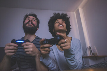 Young multiethnic couple bedroom playing videogame