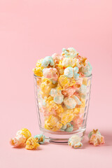 Multicolor sugary popcorn in glass  on a pink background with copy space
