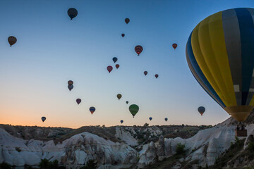 Hot air balloons flying over bizarre rock landscape in Cappadocia. Balloons fly early in the...