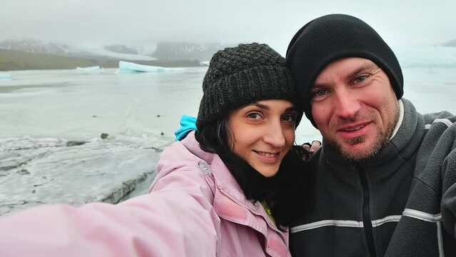 Happy influencers couple taking selfie by glacier lagoon in Iceland. Two tourists having fun on romantic winter vacation in Iceland - Holidays and traveling lifestyle multiethnic