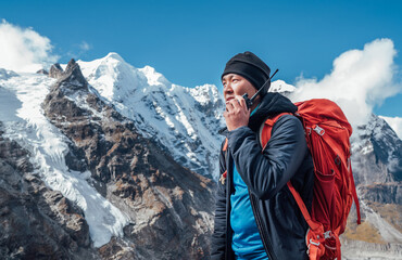 Portrait of Sherpa man with backpack using walkie-talkie for calling rescue helicopter with Mera peak 6476m background.High Himalayas expedition during mount climbing. Traveling, active people concept