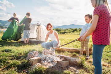Three sisters have picnic, roasting marshmallows and candies on sticks over campfire flame while...