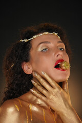 Portrait of female model in studio. Close shot pretty girl in tiara body covered in golden paint...