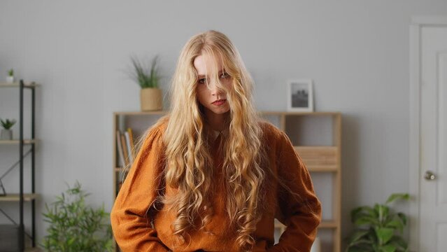 Woman blowing off a strand of hair and showing disbelief, annoyed by the trouble in the apartment of a modern house. Portrait of a girl in the living room sitting on a sofa