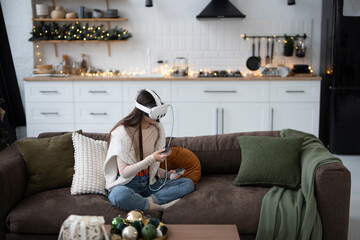 In a cozy holiday ambiance at home, a fashionable young lady uses a virtual reality headset.