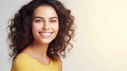A close-up of a woman with a cute smile who appears flirty to the camera, touching her cheeks and blushing while standing on a white wall in a yellow shirt.