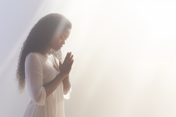 Pretty young African american woman praying to god with her eyes closed and clasped hands - profile side angle - God's rays of light shining down - Ethnic diversity and religion concept