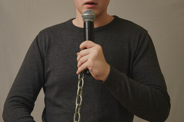 A young man holds a microphone with a steel chain instead of a wire. Restriction of freedom of...