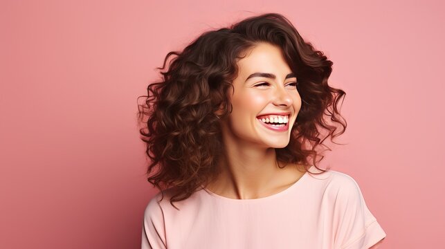 Inside, a cute and beautiful woman with wavy hair is laughing while taking an indoor photo in a pink blouse.