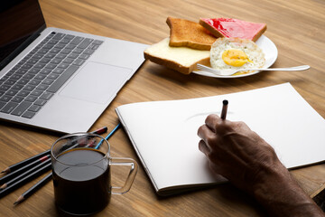 Office table desk. Workspace with blank, office supplies, laptop, eyes glasses, hot black coffee cup and butter bread sunny side up omlet on wood background.