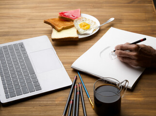 Office table desk. Workspace with blank, office supplies, laptop, eyes glasses, hot black coffee cup and butter bread sunny side up omlet on wood background. - obrazy, fototapety, plakaty