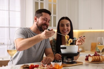 Fototapeta na wymiar Affectionate couple enjoying cheese fondue during romantic date in kitchen