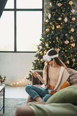 Obraz premium Enjoying a festive Christmas atmosphere at home, a stylish young woman is in a virtual reality headset.