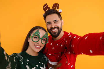 Happy young couple in Christmas sweaters, reindeer headband and party glasses taking selfie on...