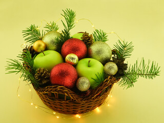 New Year's composition of fir branches, green apples, Christmas tree red and gold balls. Winter decorations for the interior. Fruit basket on yellow background.