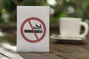 No Smoking sign and cup of drink on wooden table against blurred background, closeup