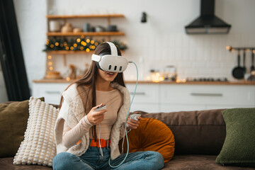 A stylish young woman in a cozy Christmas atmosphere at home, wearing a virtual reality headset.