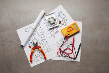 Wiring diagrams, digital multimeter, pliers, and disassembled light switch on grey table, top view