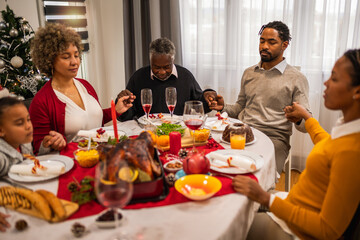 Family praying before eating delicious Christmas dinner.