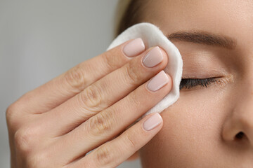 Woman removing makeup with cotton pad on grey background, closeup