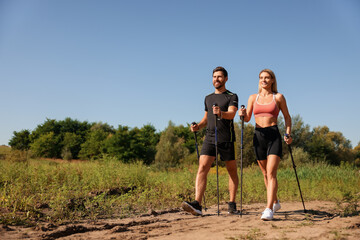 Happy couple practicing Nordic walking with poles outdoors on sunny day - Powered by Adobe