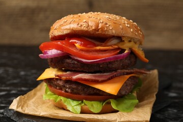 Delicious burger with meat cutlets, bacon, cheese, vegetables and lettuce on black table, closeup