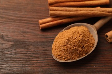Spoon with cinnamon powder and sticks on wooden table, closeup. Space for text