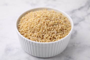 Raw bulgur in bowl on marble table, closeup