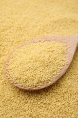 Wooden spoon and uncooked organic couscous as background, closeup