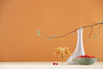 Composition with tree branch, autumn leaf and red berries on white table against orange background, space for text
