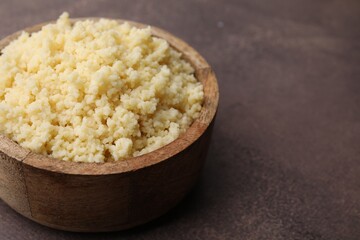 Tasty couscous in bowl on brown table, closeup. Space for text