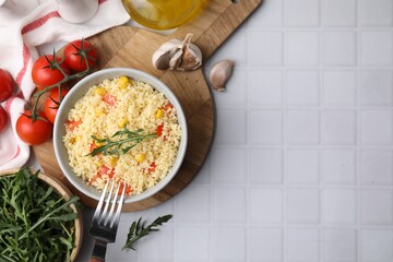 Tasty couscous with pepper, corn and arugula served on white tiled table, flat lay. Space for text